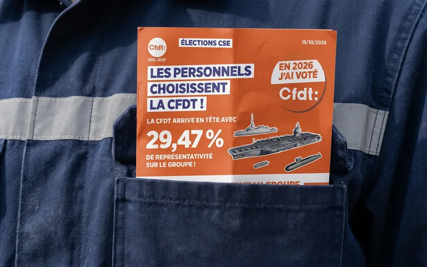 Grande bâche d’affiche sur une façade haussmannienne : un ouvrier vu de dos, un slogan en capitales, trois revendications.