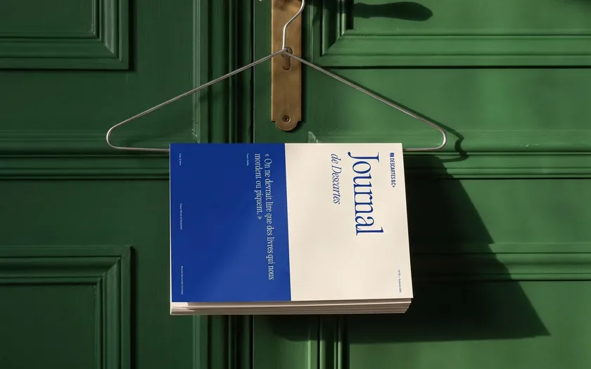 Un journal à couverture bleue et blanche, glissé sur un cintre accroché à une porte vert foncé.