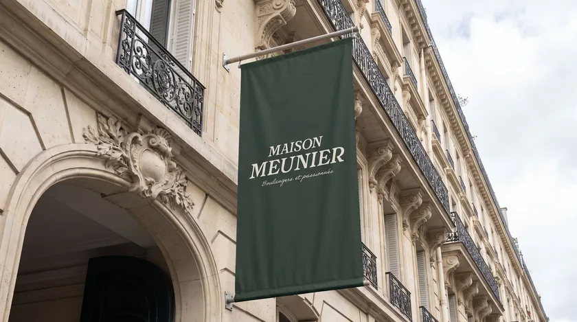 Bannière vert sombre suspendue à une façade haussmannienne, le nom de la maison en lettres dorées.